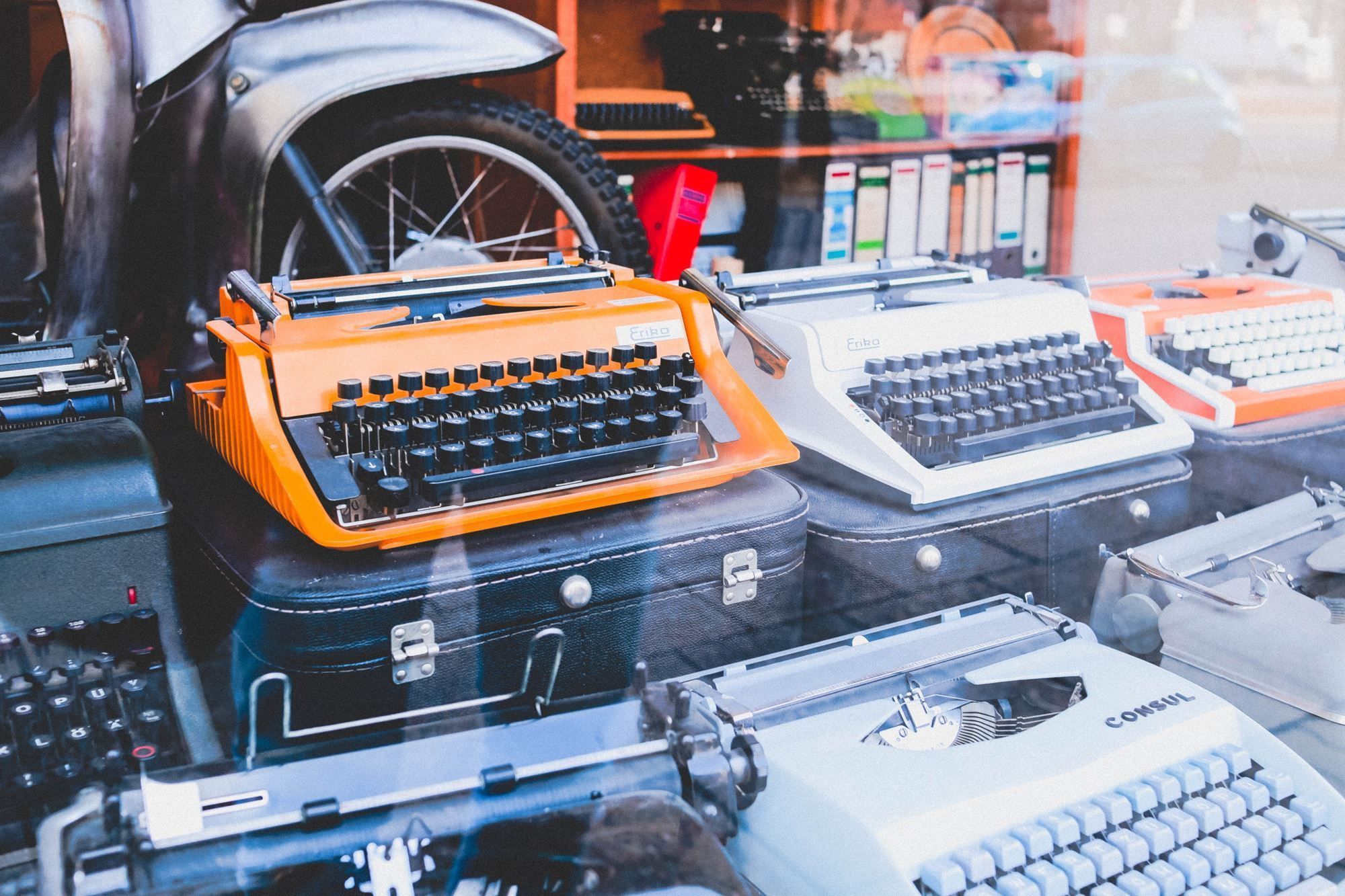 An orange typewriter sitting next to other old typewriters behind glass