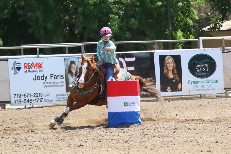 Teen girl in a green plaid shirt on a horse barrel racing at the Colorado State Fair
