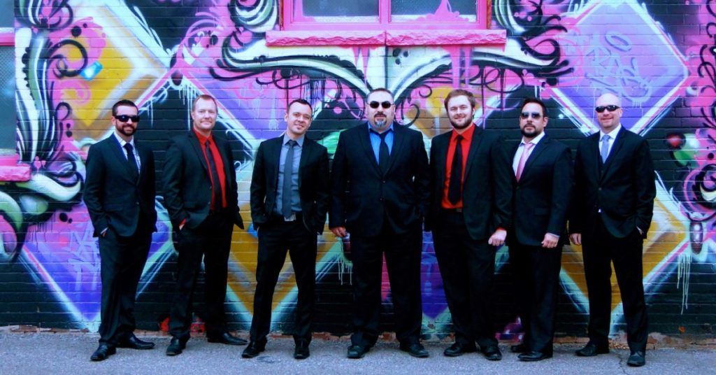 Martini Shot band photo wearing suits and sunglasses in front of pastel designs on a wall