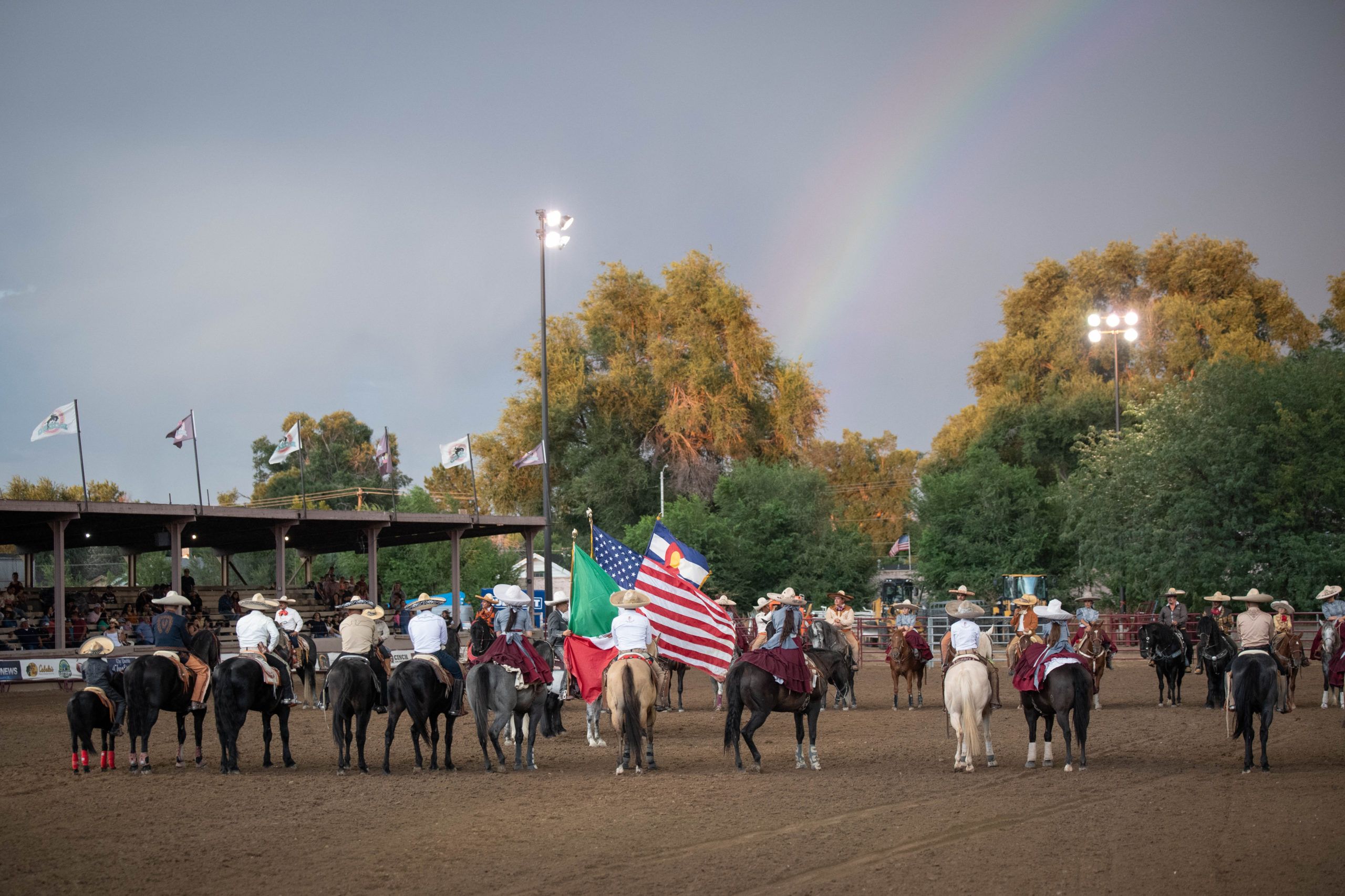 People riding horses in a line and holding flags