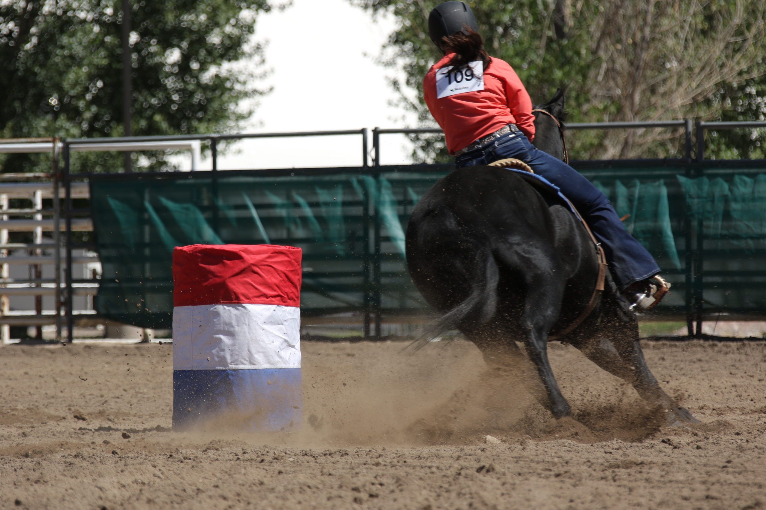 A cowgirl in a red shirt barrel racing at the Colorado State Fair