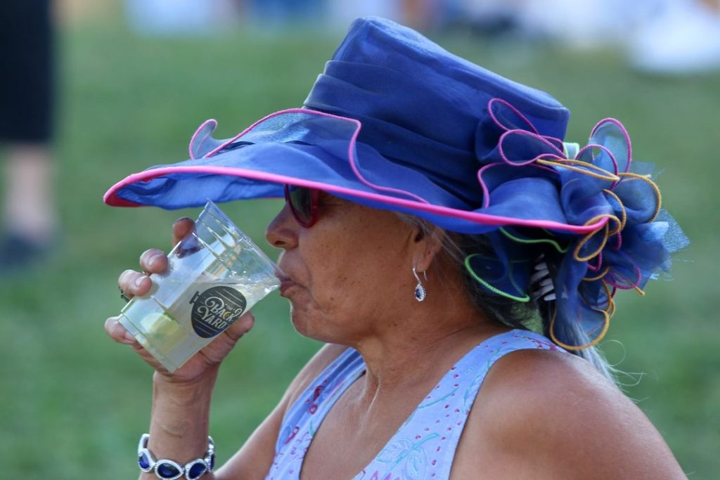 A woman with a beautiful blue hat drinking a refreshment on a hot day at the State Fair