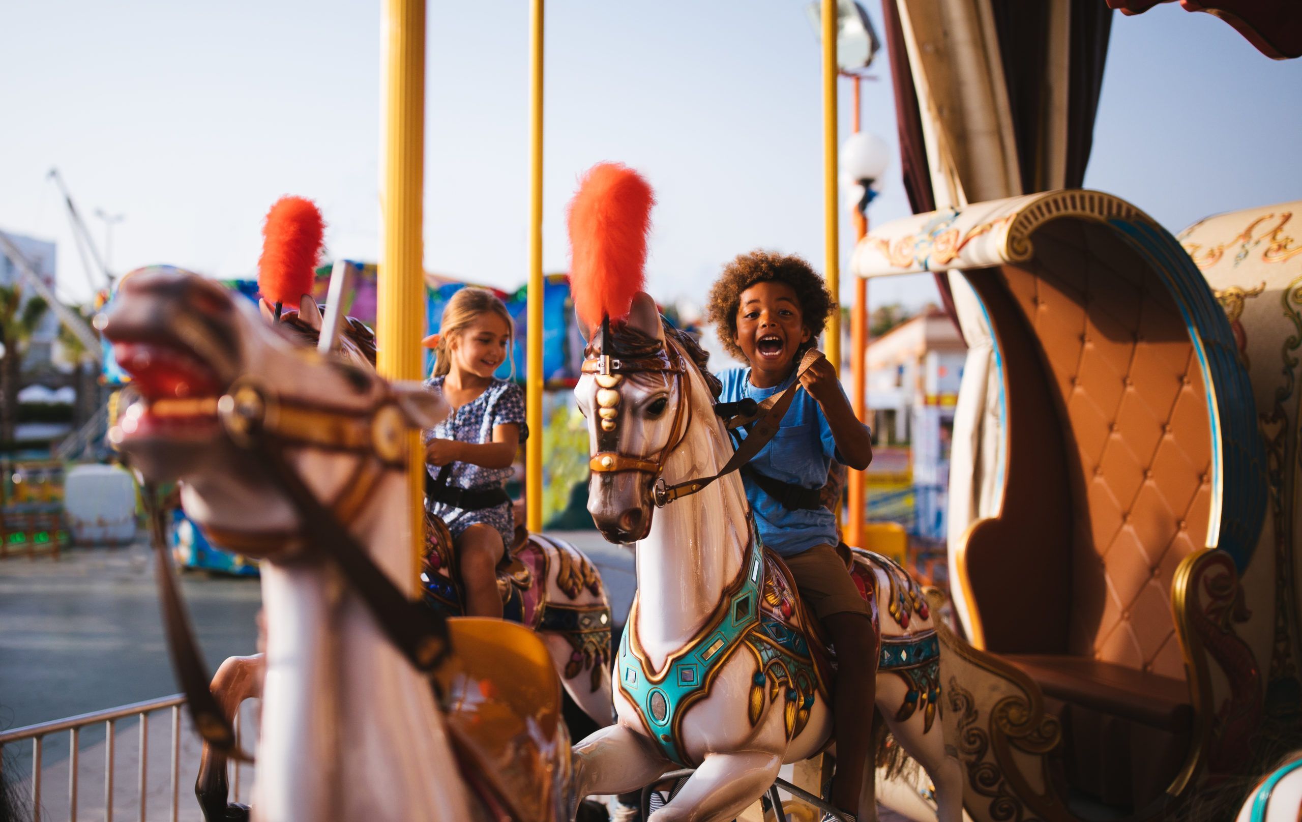 Multi-ethnic mixed family brother and sister having fun riding horses on amusement park carousel ride
