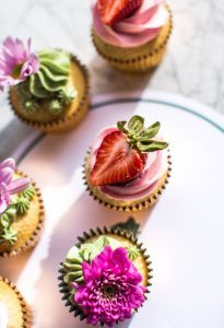 Strawberry and flowers sitting on cupcakes as seen from above