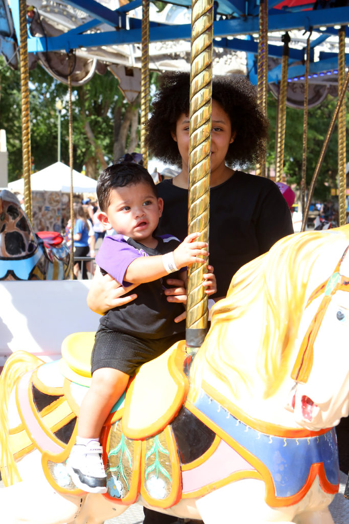 A toddler rides a carousel horse as his mother holds him