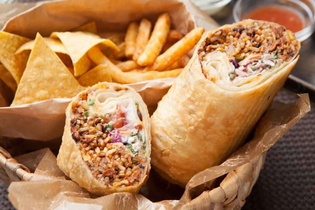 A burrito is cut in half and sits in a paper lined basket with a side of fries