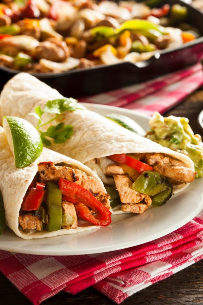 Chicken fajitas in flour tortillas with peppers and a lime wedge 