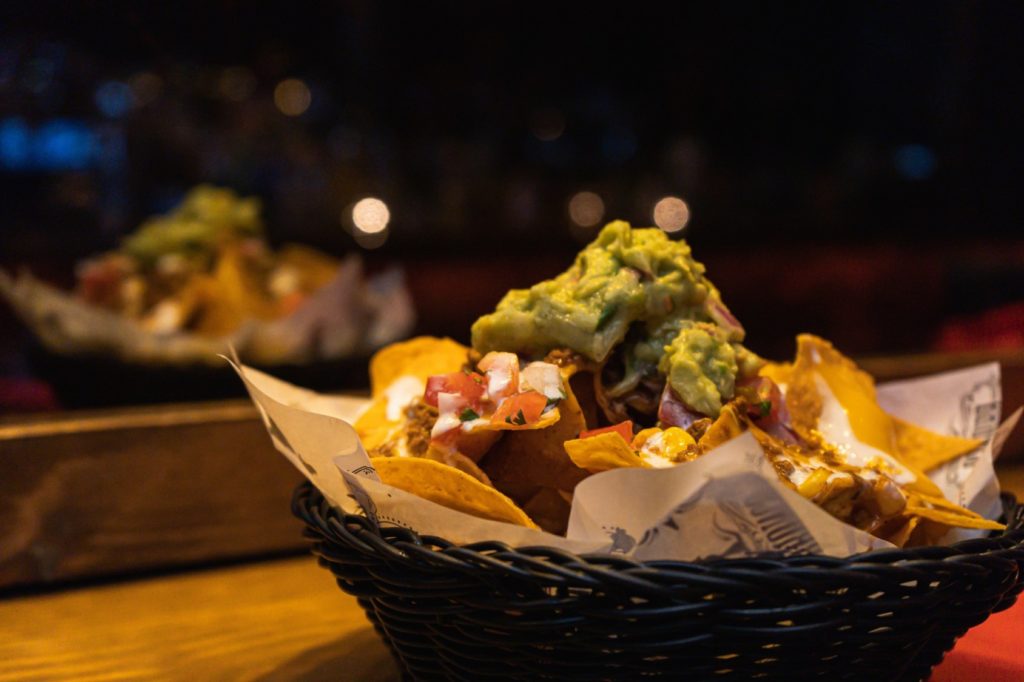 A basket is filled with warm tortilla chips topped with pico de gallo and guacamole