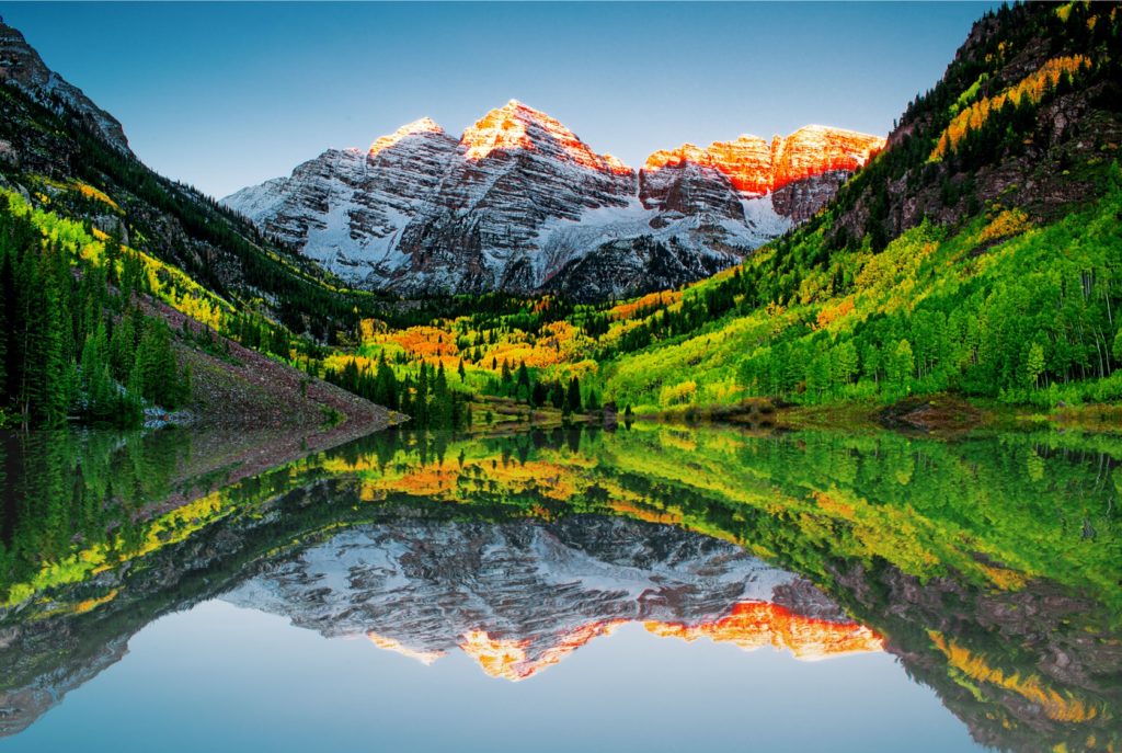 A mountain and surrounding lush foliage are mirrored in a mountain lake at sunset