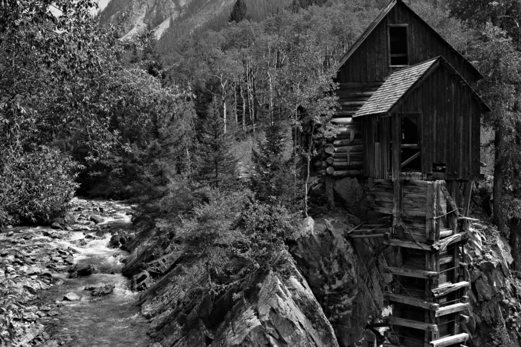 An old mill in Colorado is shown next to a creek in a black and white photograph