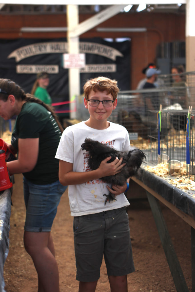 A boy in a barn holds a chicken to his chest in both arms