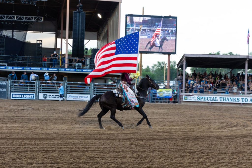 A woman rides a horse in an arena holding the American Flag