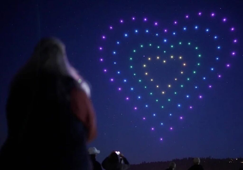 woman viewing drones in heart shape in the night sky